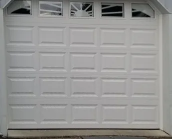 A white raised-panel garage door with a row of arched sunburst windows across the top, in a light gray steel-sided building.