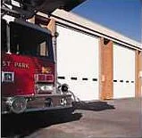 A red fire truck parked in front of a firehouse with white overhead doors.