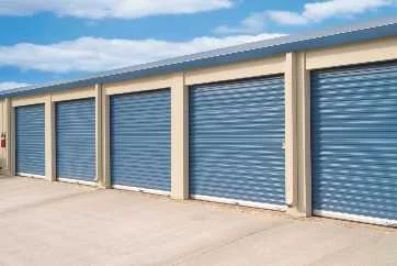 A row of blue rolling steel doors along a long one-story building.