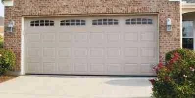 A cream double garage door with raised panels and a row of arched windows on a brick house.