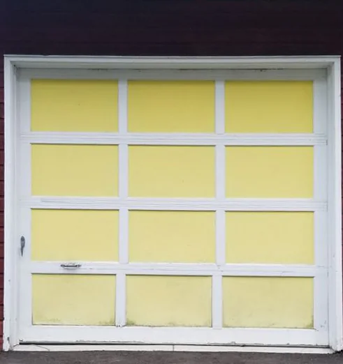A single garage door with white frames and yellow painted panels, set in dark red siding.