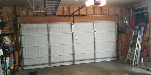 Inside a garage with wood-framed walls: an older white double door braced with vertical steel struts.