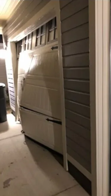 A garage door with a row of windows, photographed at a sharp angle under artificial light, its lower sections pushed out of line.